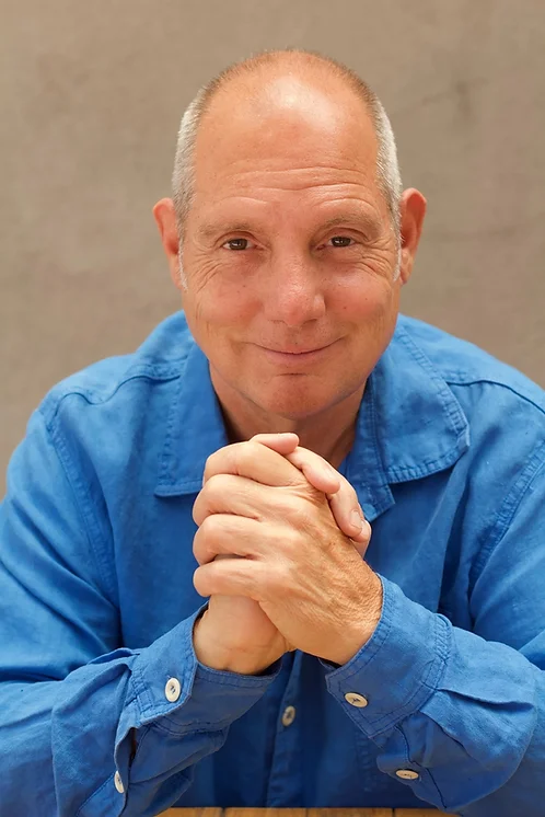 Robert Colt in a blue shirt, hands clasped, smiling warmly